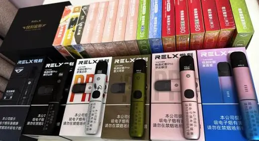 A shelf row of sealed RELX pod cartons in multiple flavor colors, with boxed devices in front