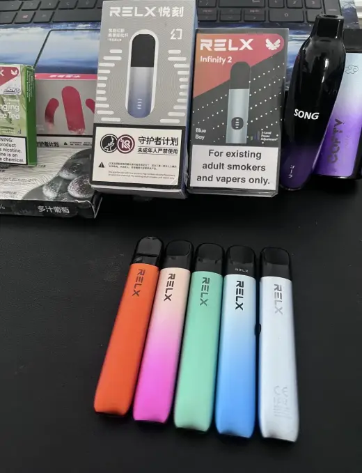 A black RELX retail box with five branded devices and spare pods laid out in front